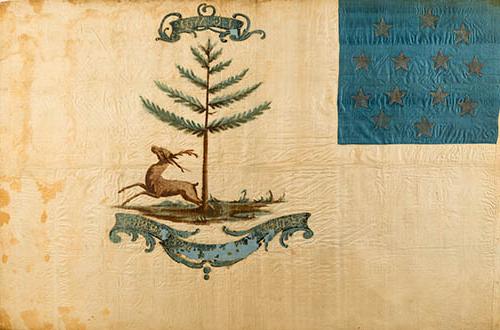 <p>A flag painted on yellowing white silk, somew帽子 worn. In the upper lefthand corner is a square of blue silk with 13 stars arranged in a circle. In the center is a bounding stag beneath a pine tree. A large cartouche underneath, slightly peeling, reads “The Bucks of America,” smaller cartouche at the top of the image has the initials “J-G-W-H.” painted in gold.</p>